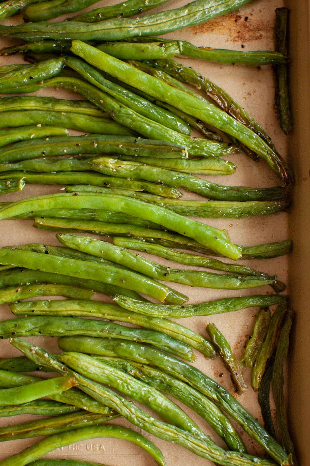 Overhead shot of roasted green beans in a baking dish seasoned with oil, salt, and pepper.
