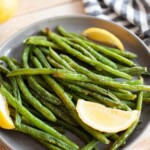Oven-roasted green beans on a plate with lemon slices.