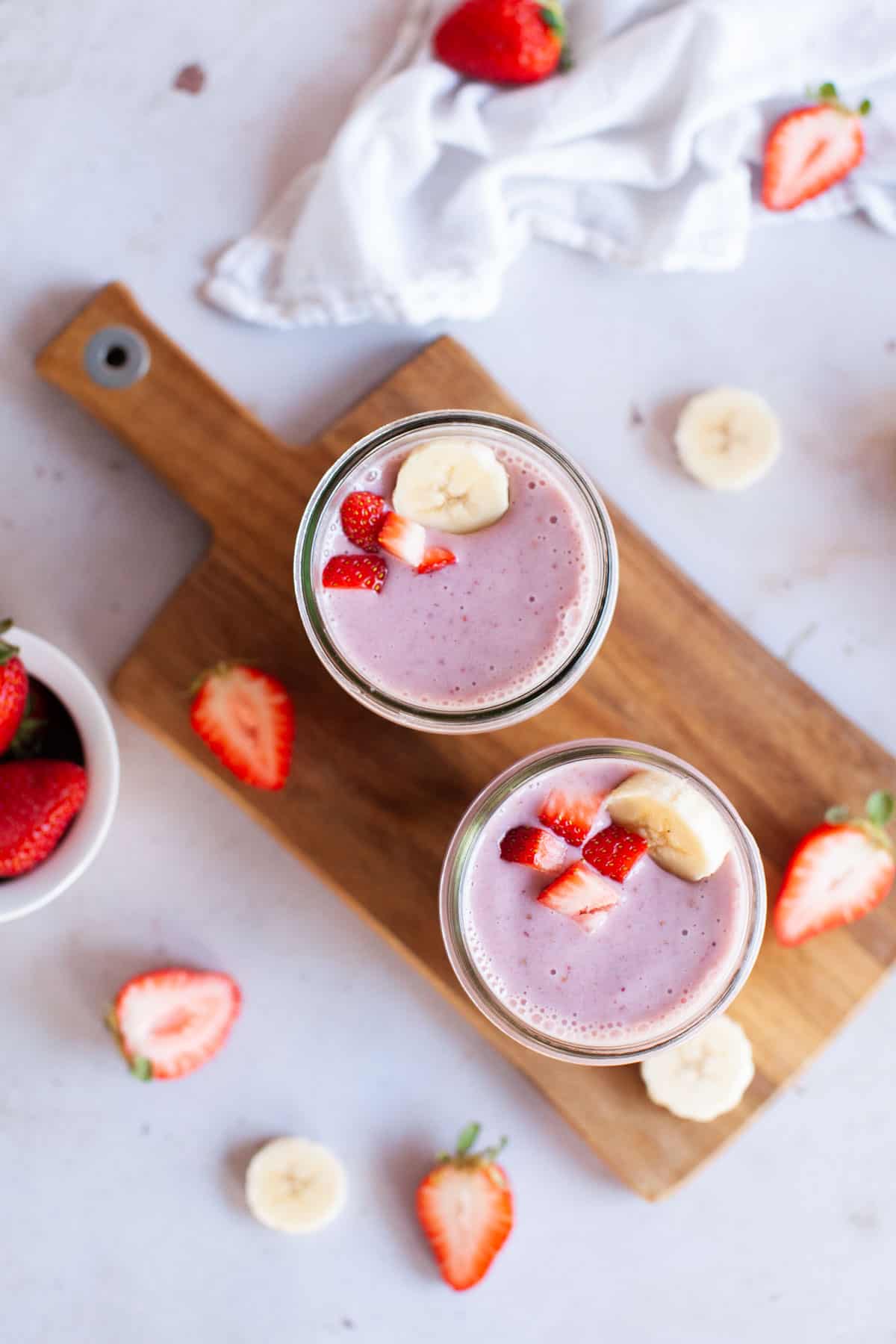 Overhead shot of two strawberry smoothie jars on top of wooden serving board.