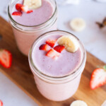 Beauty shot of two smoothie glasses filled with strawberry banana smoothie and topped with chopped strawberries and a banana slice.