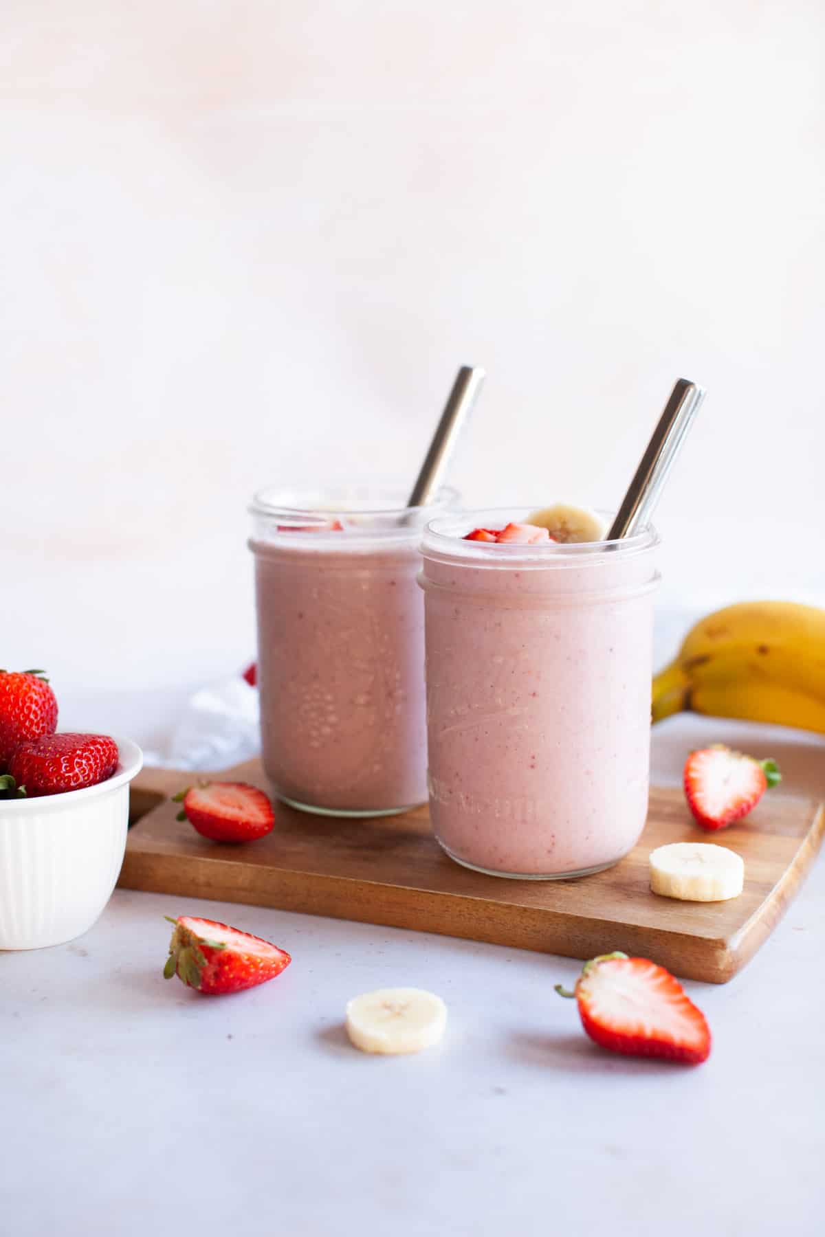 Two glass jars full of strawberry banana smoothie. Sliced strawberries and bananas around glasses.