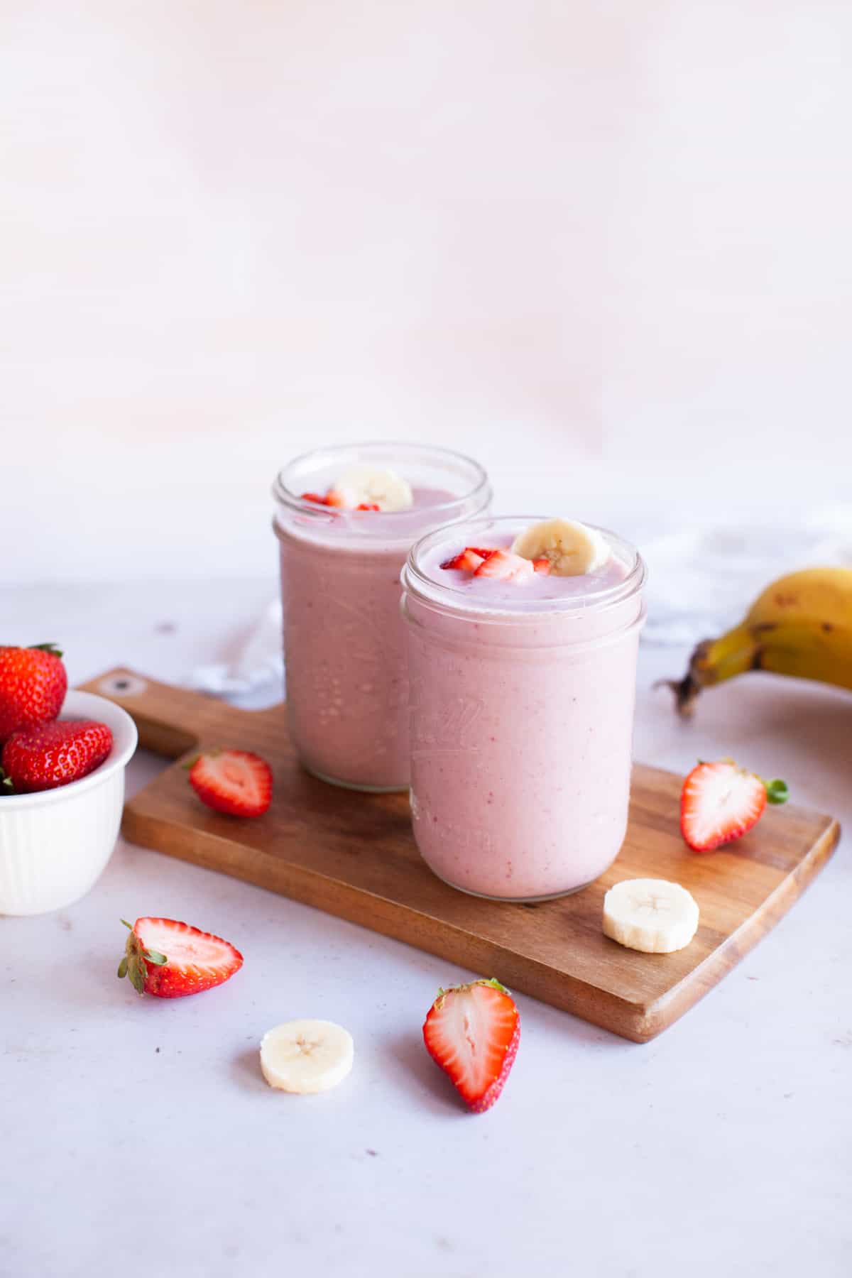 Glass jars with strawberry smoothie and sliced fruit around jars.