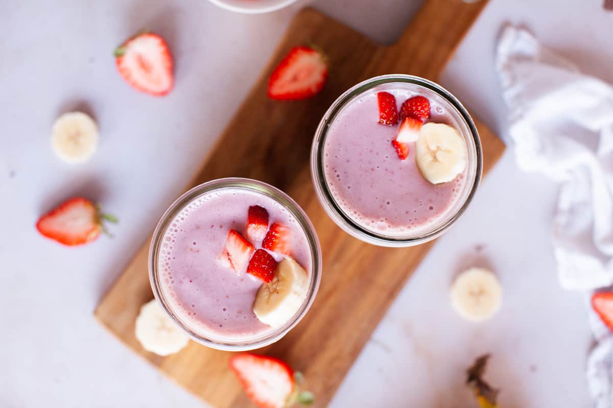 Overhead shot of smoothies in glass jars with wooden board underneath.