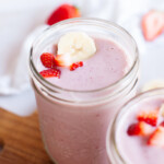Beauty shot of smoothie in glass jar with strawberries and bananas on top.