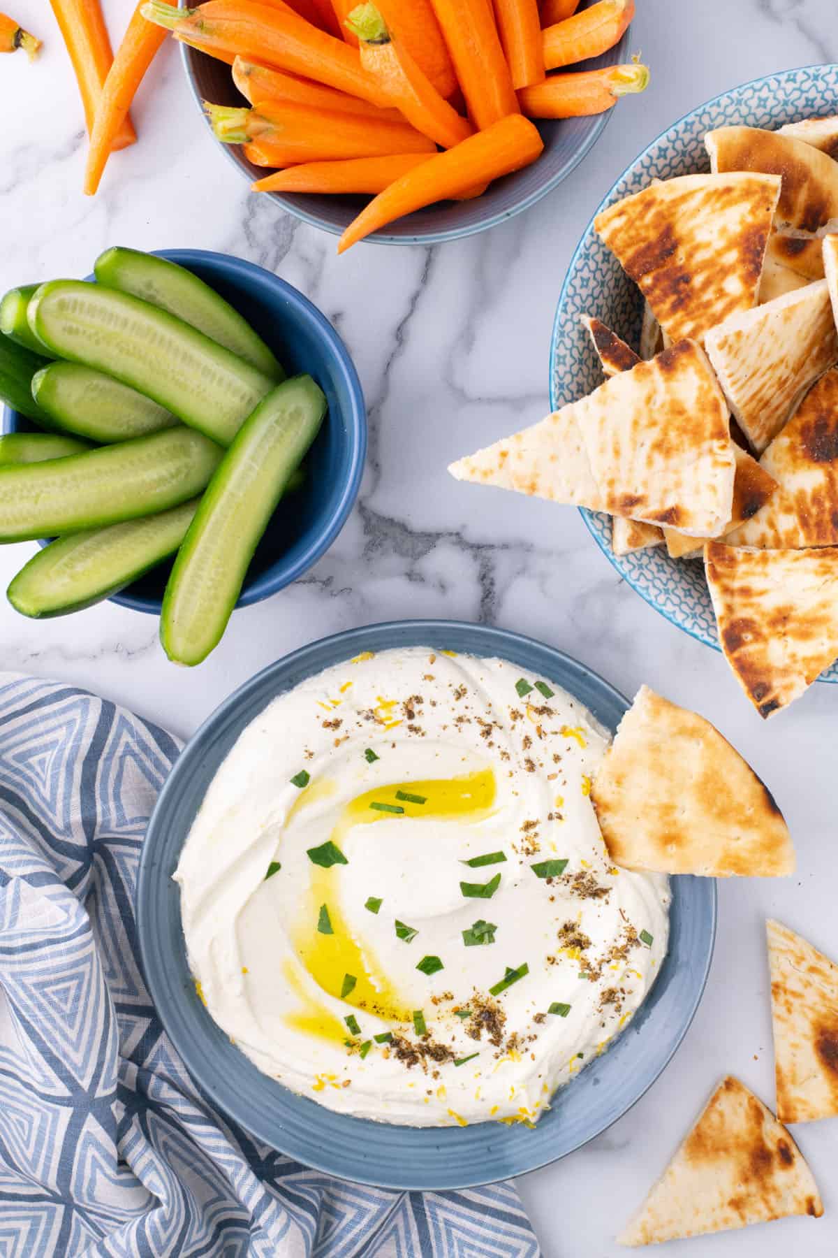 Whipped feta dip in a serving bowl, surrounded by cucumber spear, carrot sticks, and pita bread.