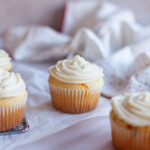 vanilla icing is piped on vanilla cupcakes.