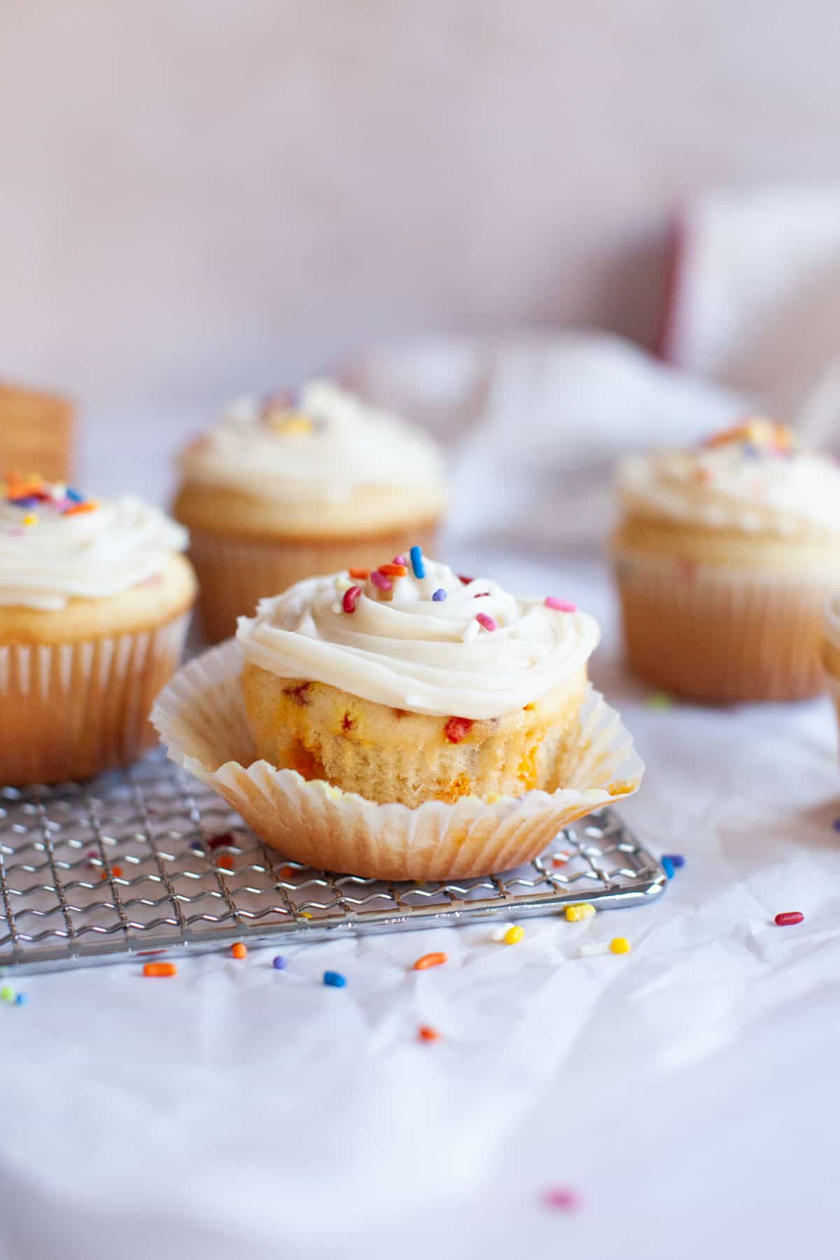 confetti cupcakes in an open muffin wrapper on a cooling rack.