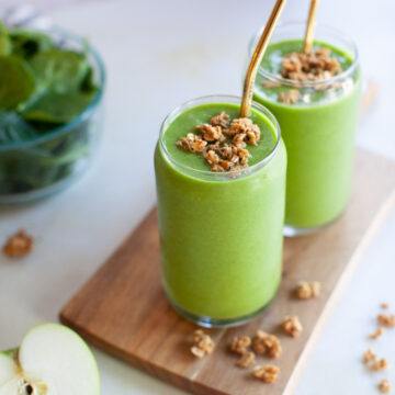 granola on top of a green smoothie with a copper straw
