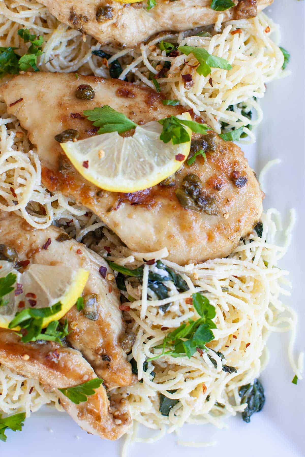 Lemon slices on top of chicken piccata, sitting on a bed of angel hair pasta.