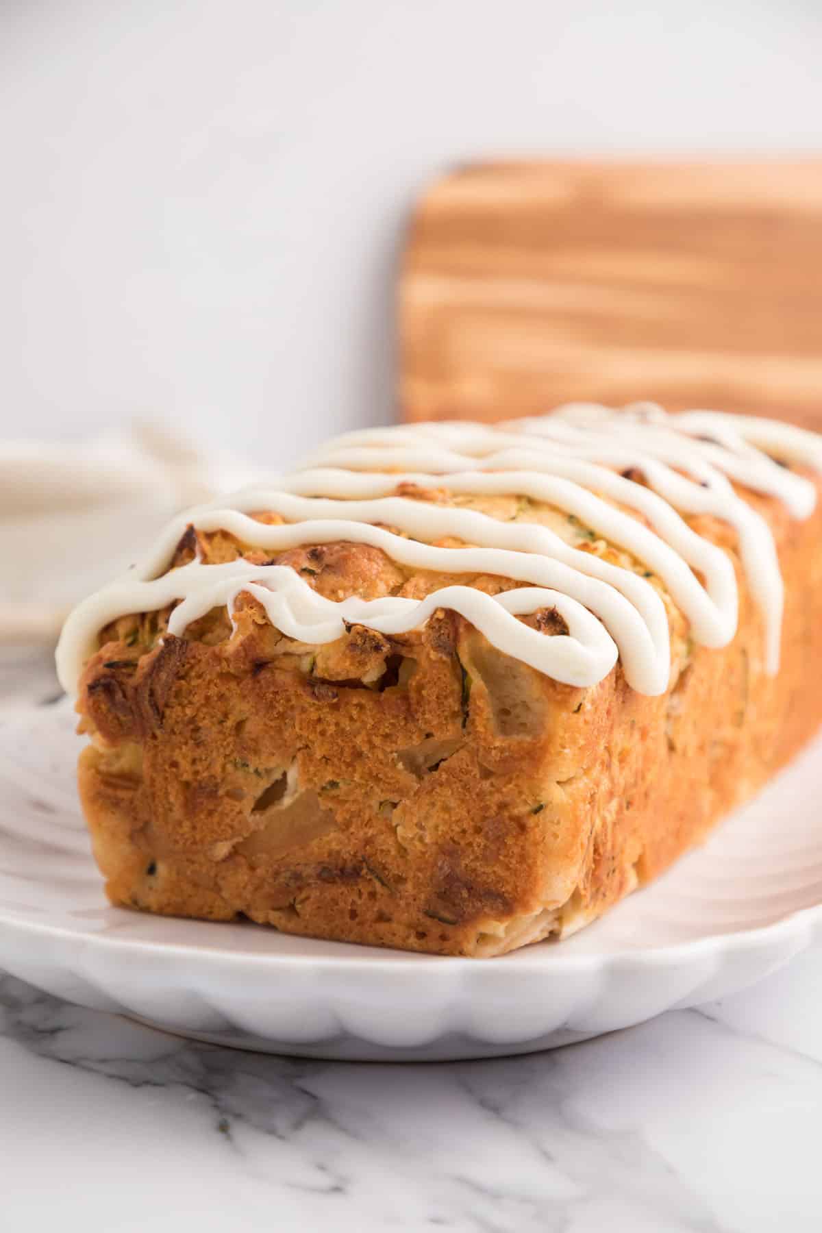 Close-up photo of baked apple zucchini bread with cream cheese glaze in an oval serving dish.