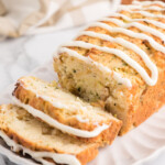 Close-up photo of baked apple zucchini bread with cream cheese glaze in an oval serving dish. The loaf has two slices cut from it.