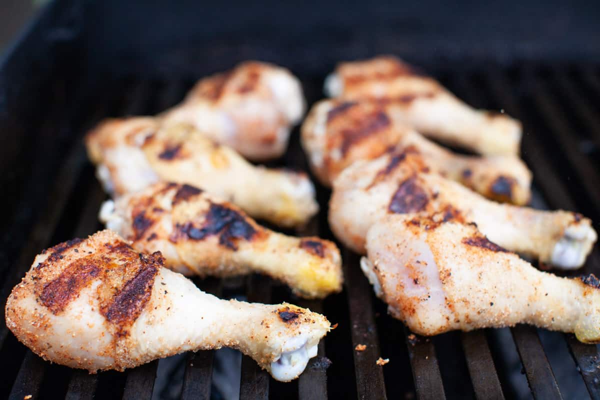 Seasoned chicken drumsticks being cooked on a grill.