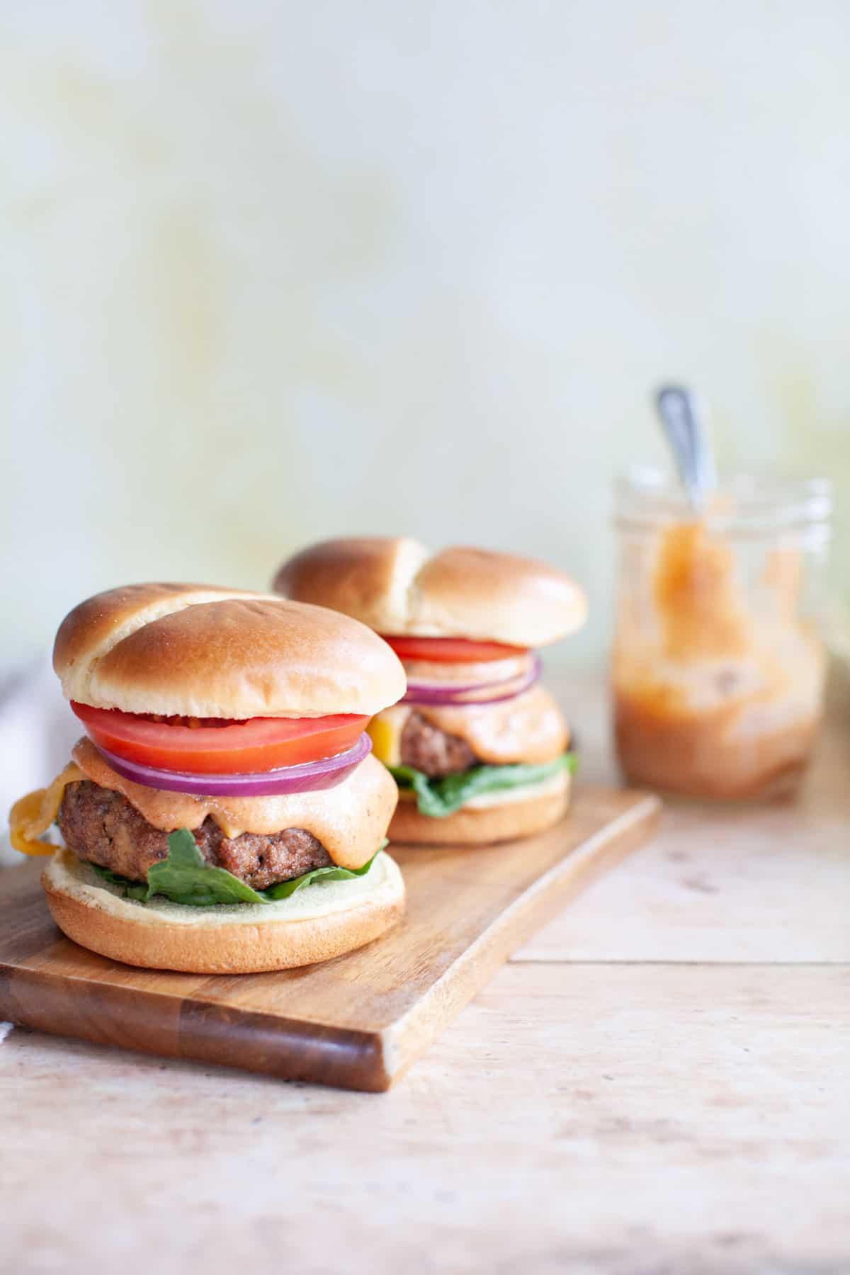 Burgers on a cutting board with burger sauce in the background.