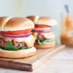 two beef burgers all the way on buns sitting on a wood board