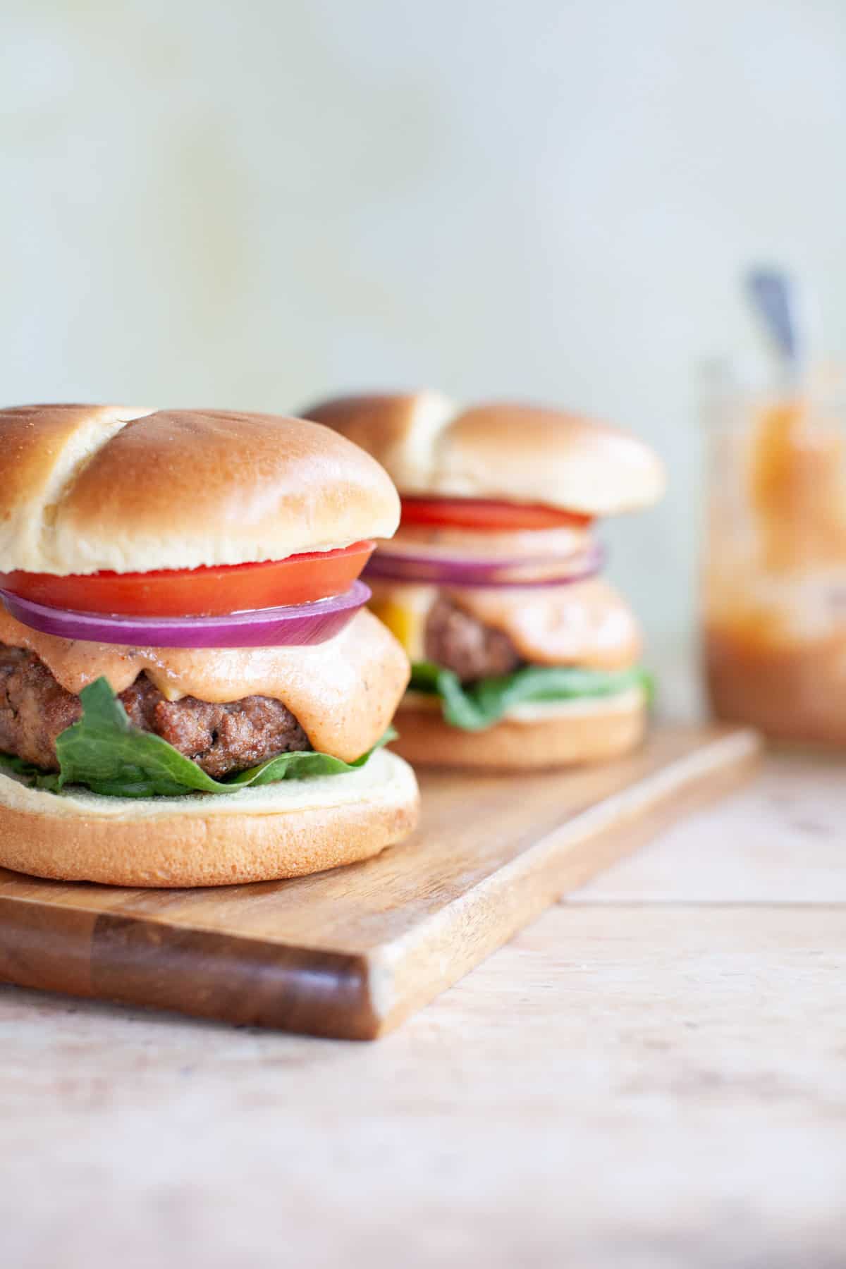 two beef burgers all the way on buns sitting on a wood board