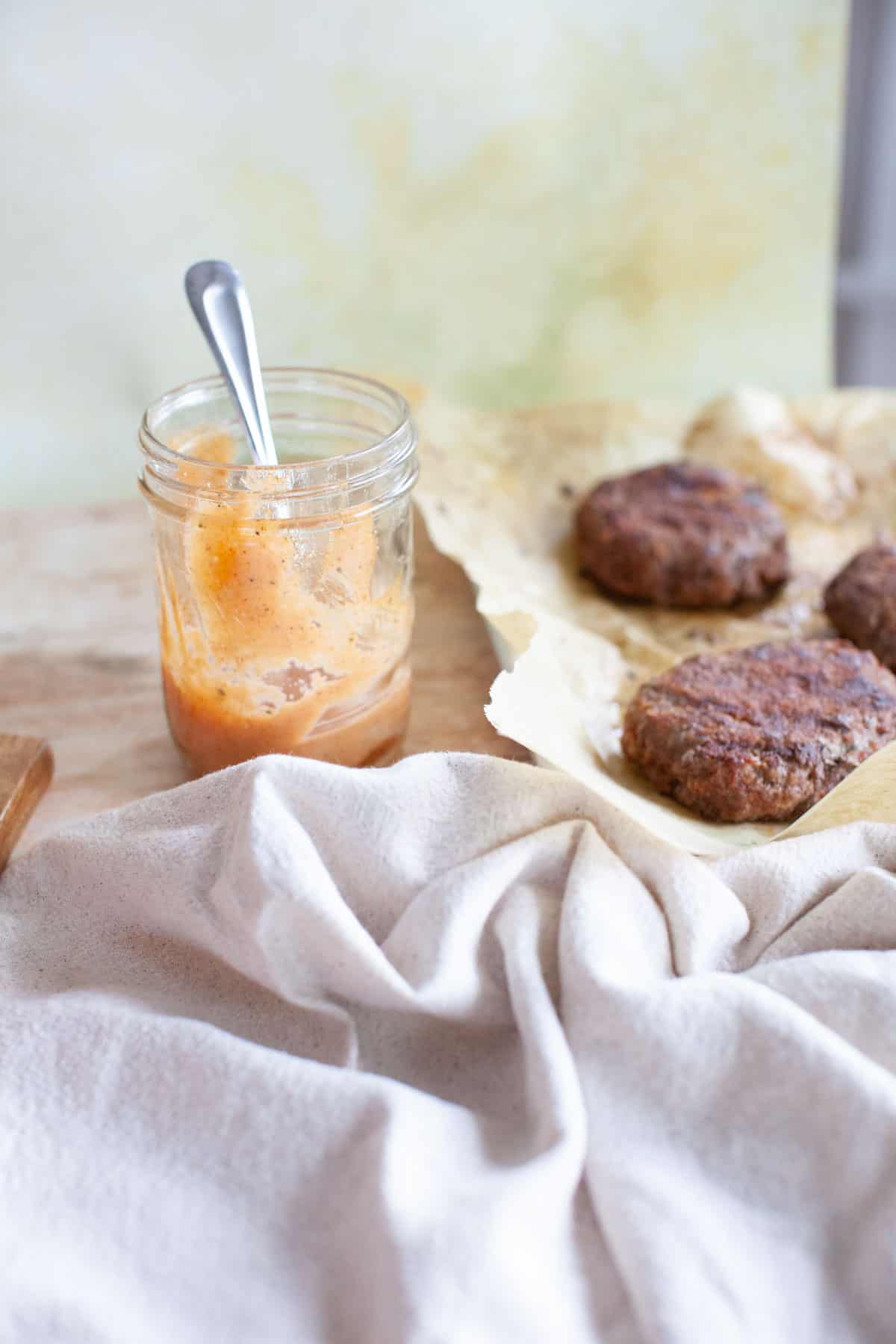 Burger sauce in a mason jar sitting next to homemade beef burger patties.