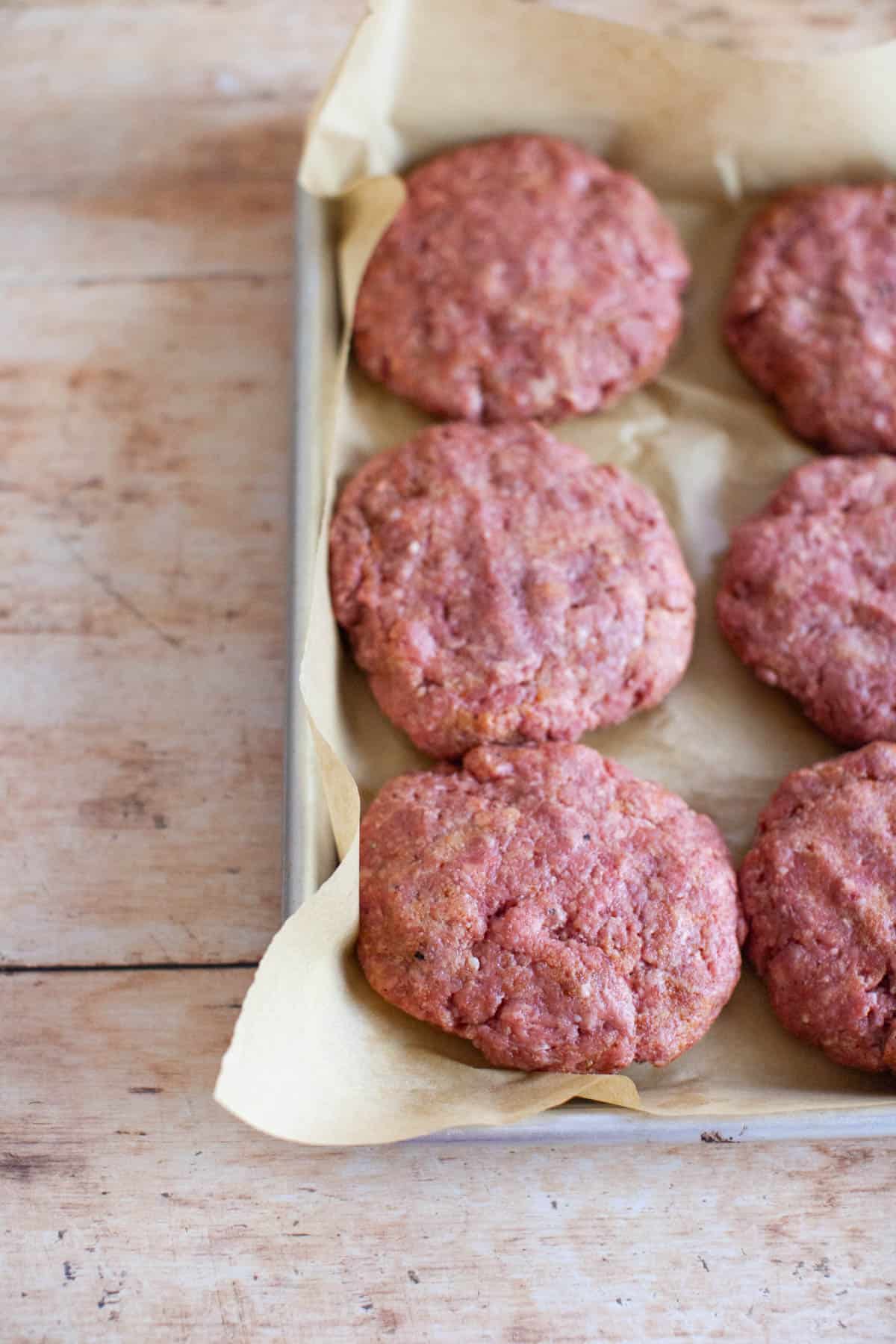 Beef burger patties on a baking sheet lined with parchment paper.