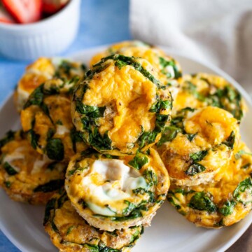 A plate of egg muffins with a bowl of strawberries in the background.