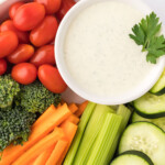 Overhead photo of homemade ranch dressing in a small white bowl placed in a larger white bowl surrounded by fresh vegetables.