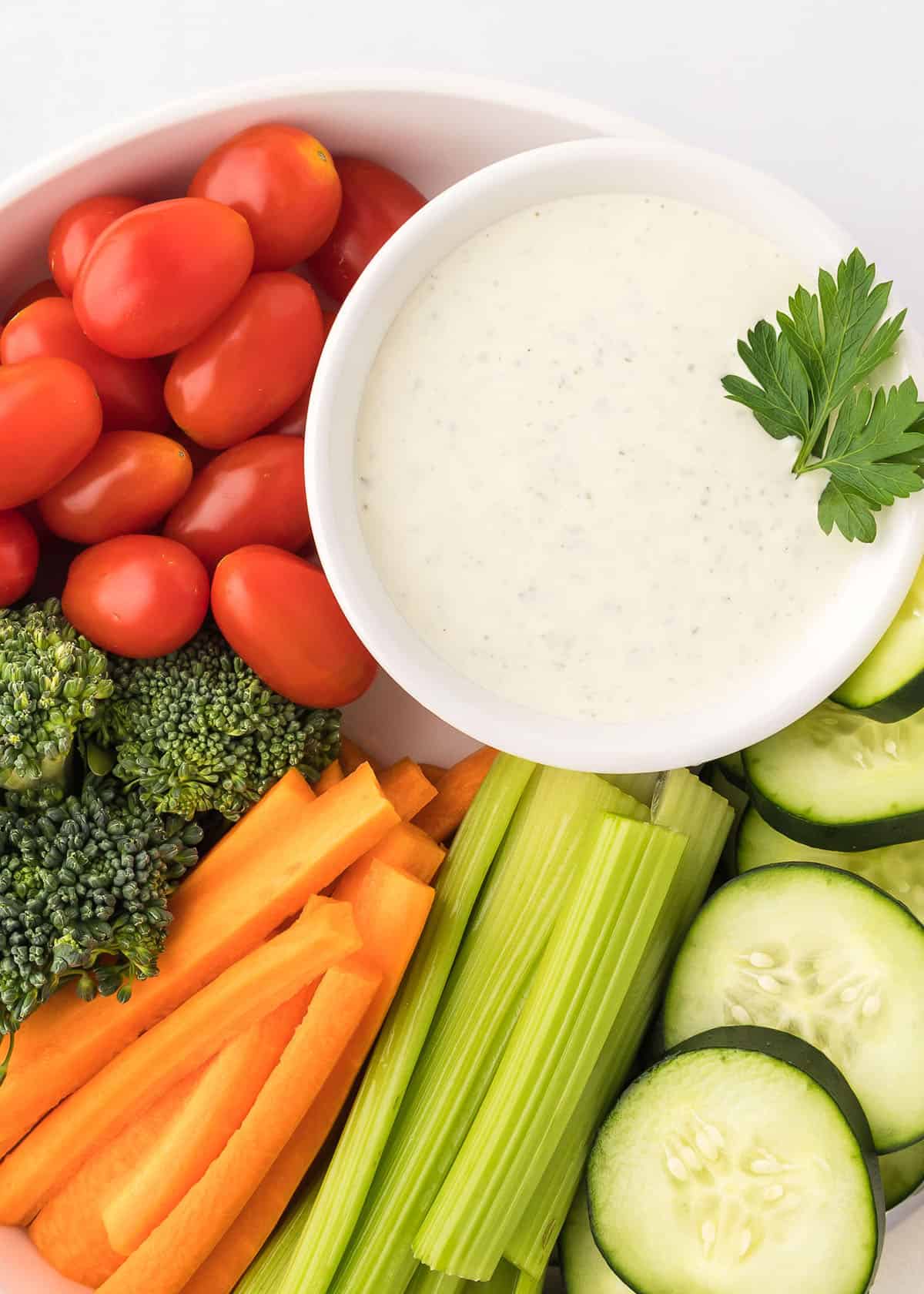 Overhead photo of homemade ranch dressing in a small white bowl placed in a larger white bowl surrounded by fresh vegetables.