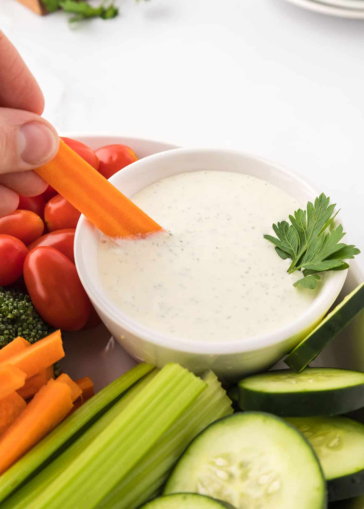 A carrot slice being dipped into the small bowl of homemade ranch dressing.