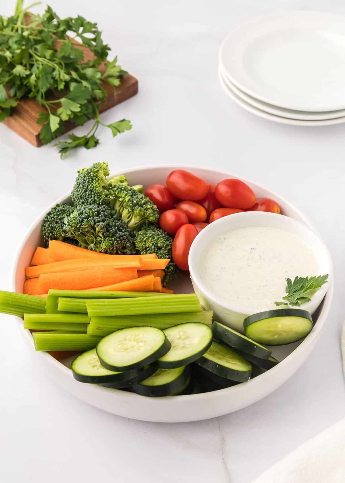 Homemade ranch dressing in a small white bowl placed in a larger white bowl surrounded by fresh vegetables.