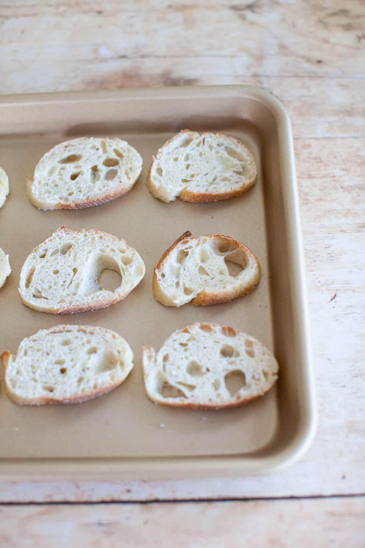 Slices of baguette on a baking sheet, sitting on a countertop