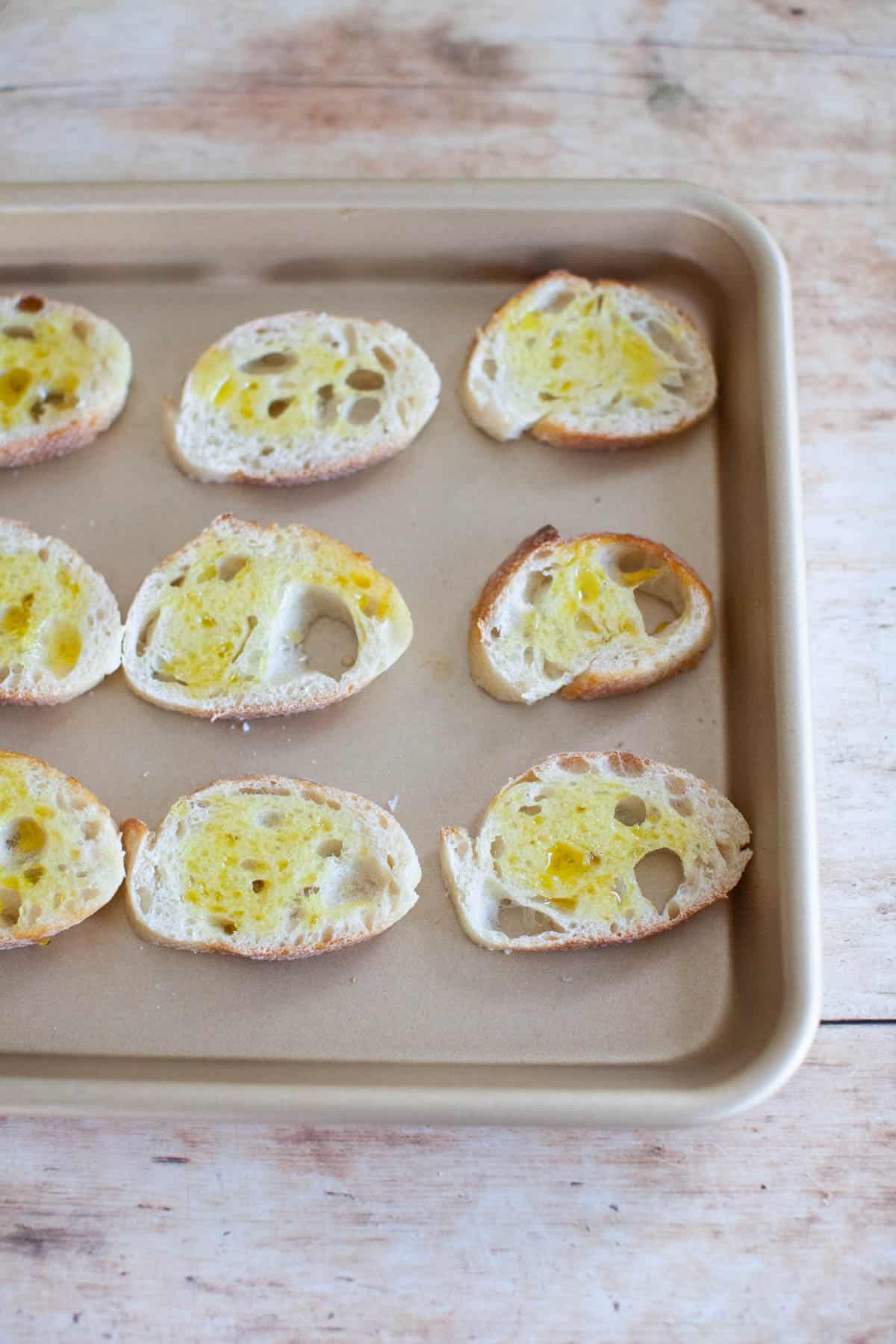 Slices of baguette, covered in olive oil, on a baking sheet