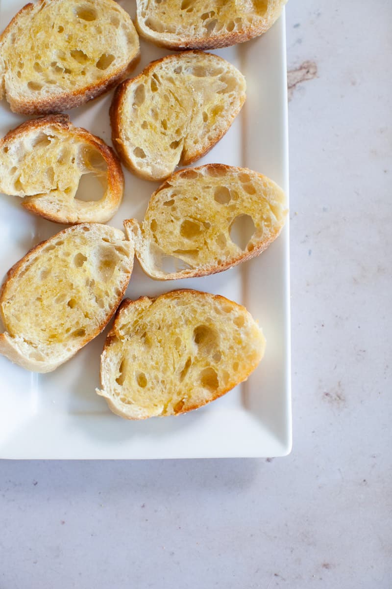 Crostini on a white platter, on a marble countertop