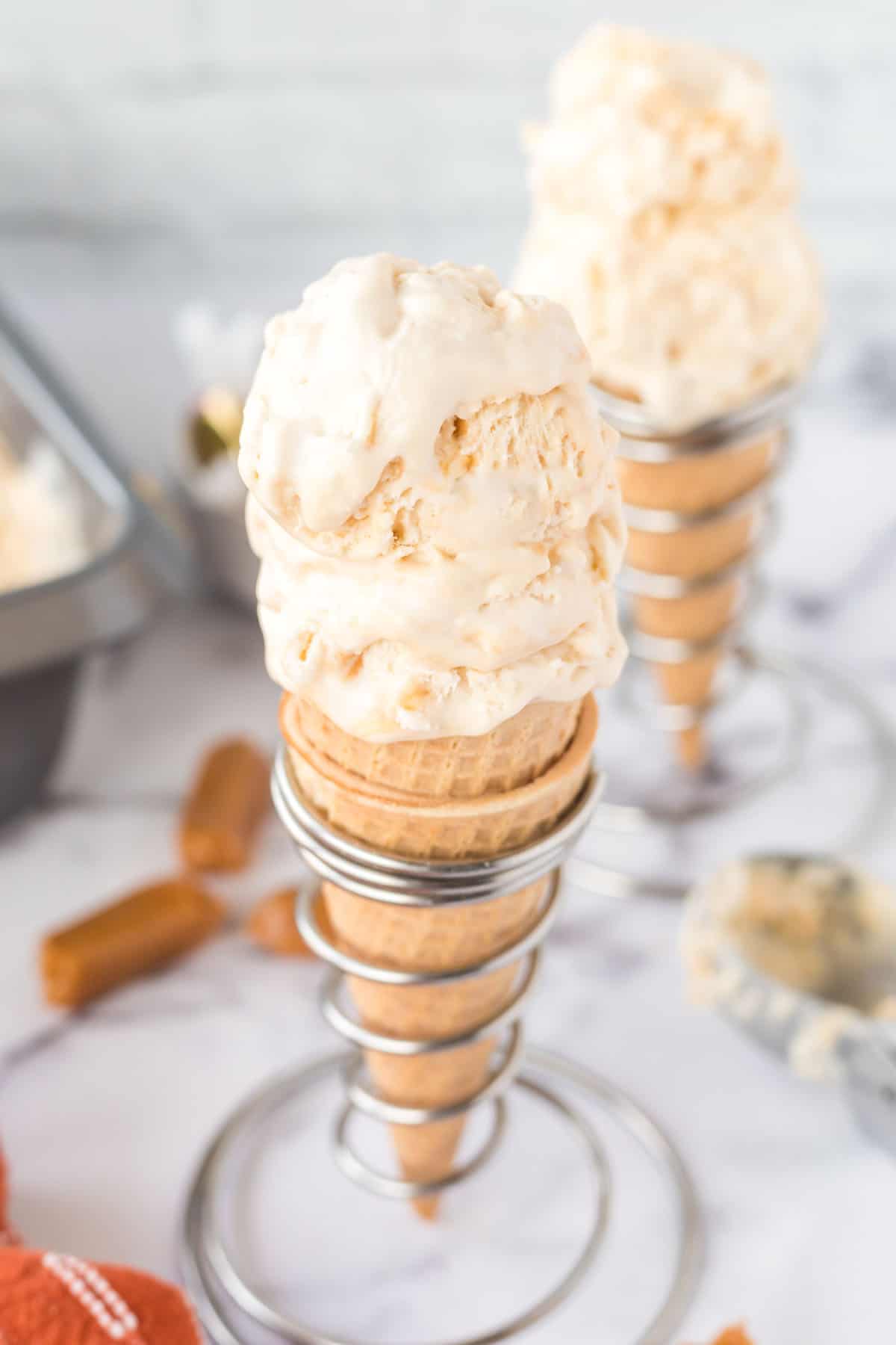 Angled overhead photo of two sugar cones in wire cone holders filled with two scoops of salted caramel ice cream.