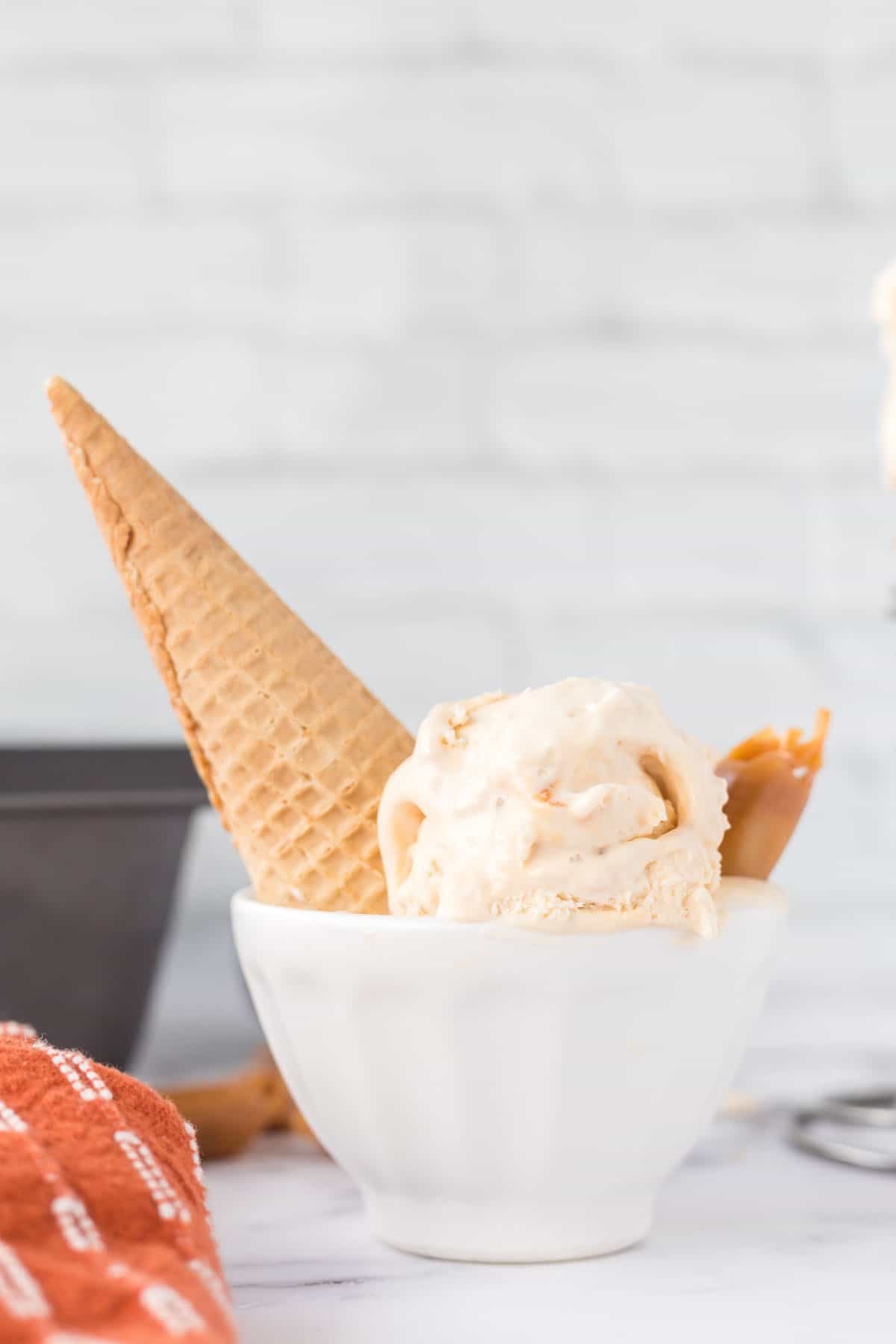 A wide-shot photo of salted caramel ice cream in a small, white bowl with a piece of caramel and sugar cone sticking out of the side of the bowl.