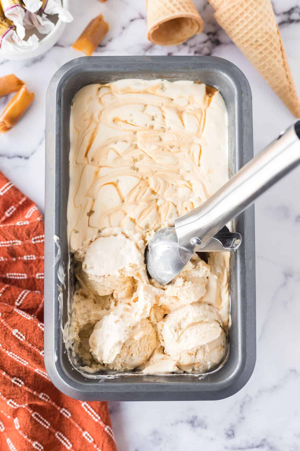 Salted caramel ice cream in a rectangular, metal serving dish with an ice cream scooper.