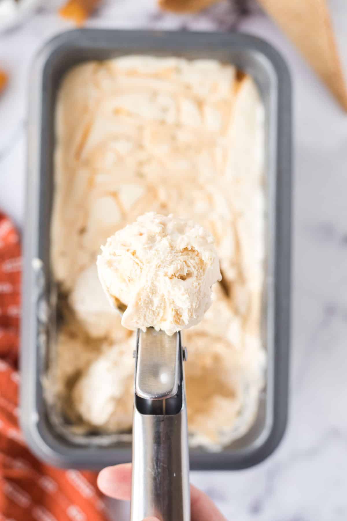 A small scoop of salted caramel ice cream in an ice cream scooper above the rectangular, metal serving dish.