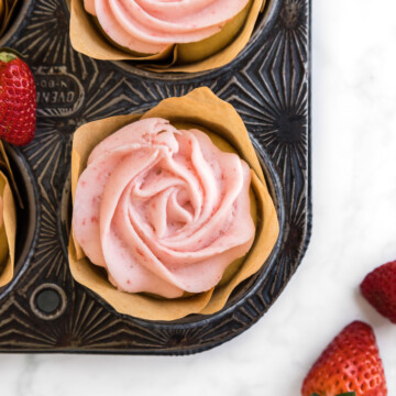 Close up shot of baked strawberry buttercream cupcake with full strawberries accenting the edges of the photo.