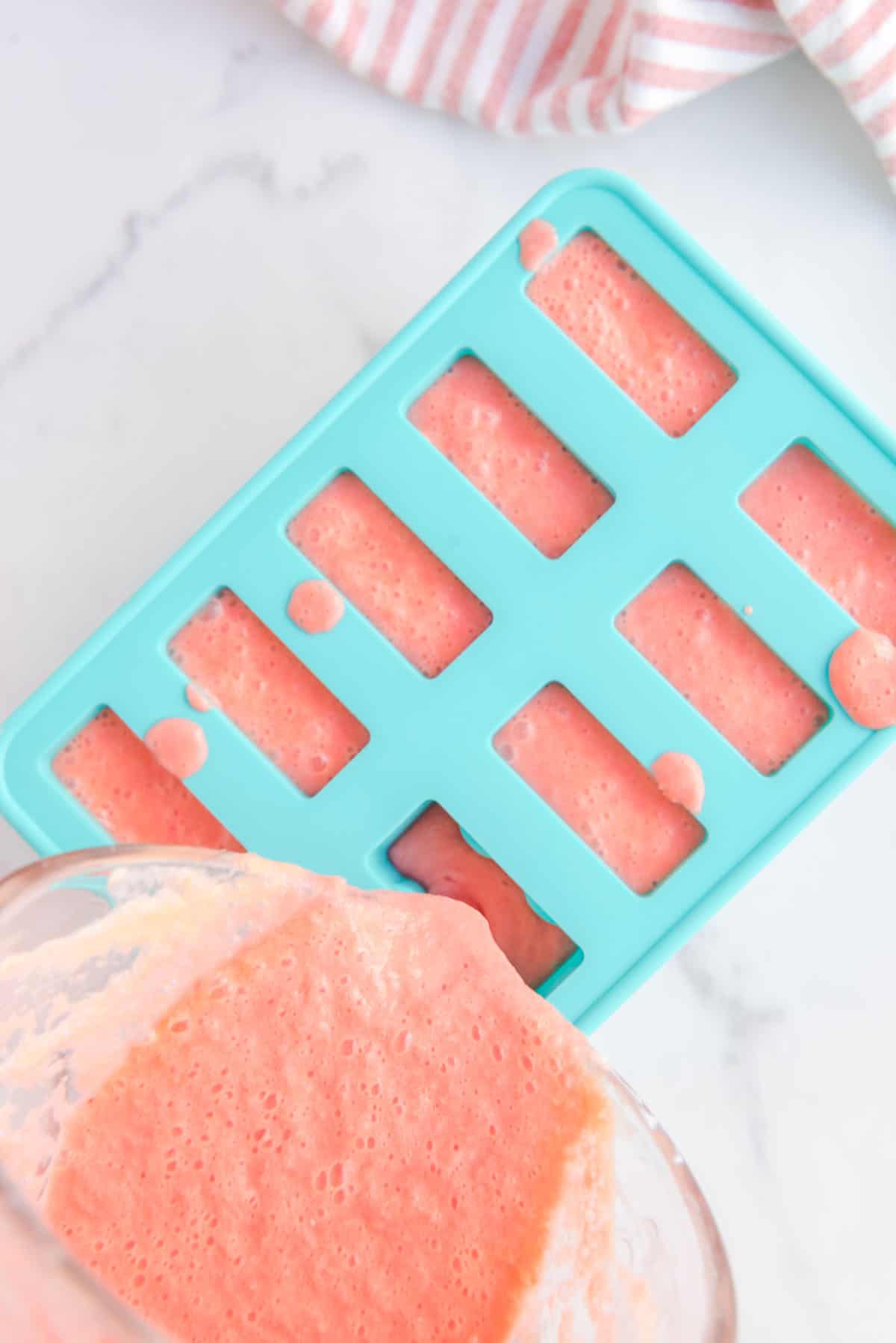 Overhead shot of blended popsicle ingredients being poured in the popsicle mold.