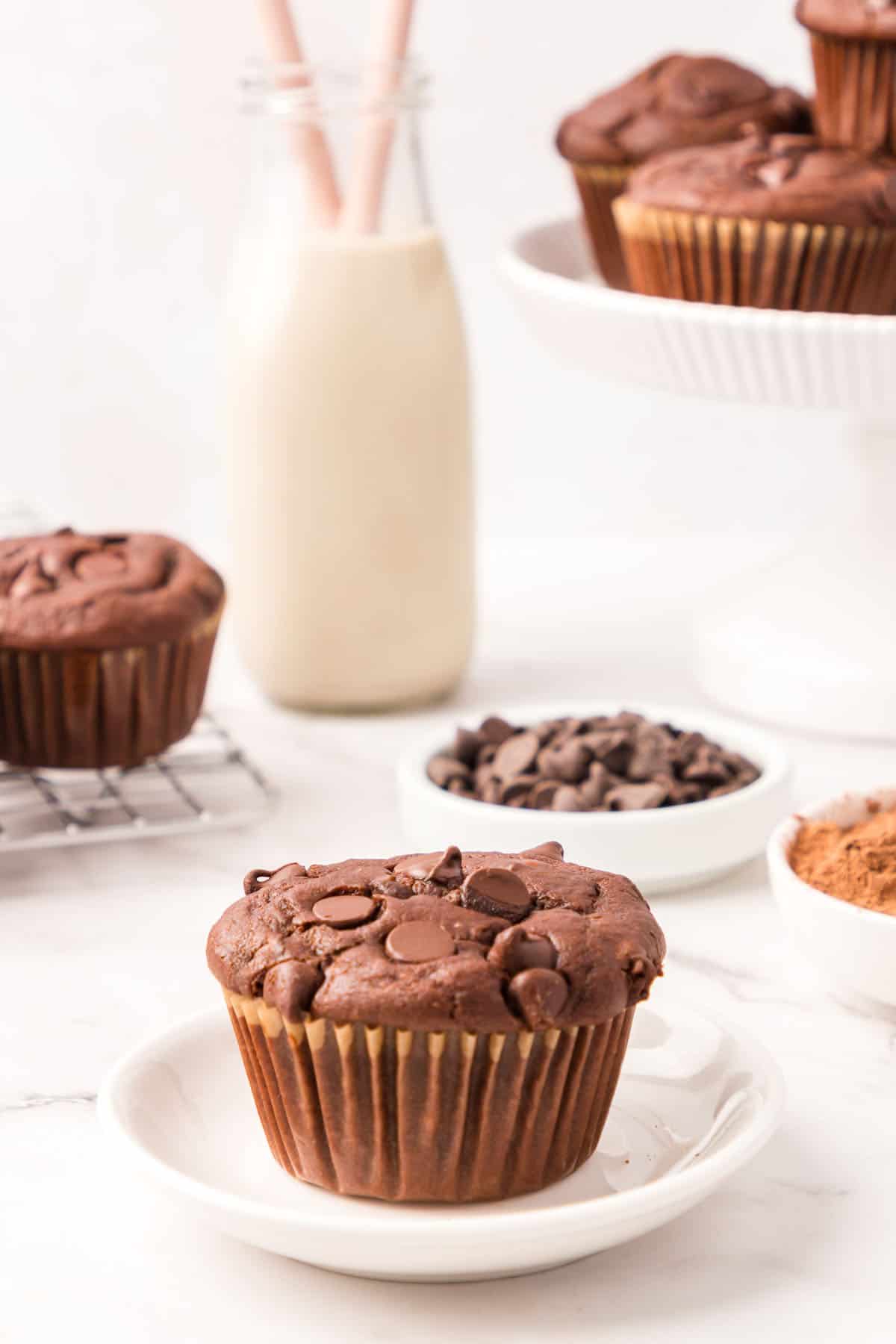 Wide shot photo of chocolate muffin on a small, white plate.