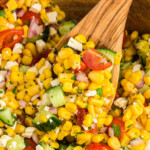 A close-up photo of the corn salad being scooped out of a wooden bowl with a wooden spoon.