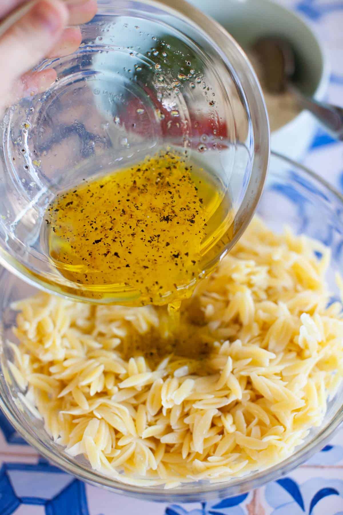 Olive oil dressing being poured onto cooked orzo pasta.