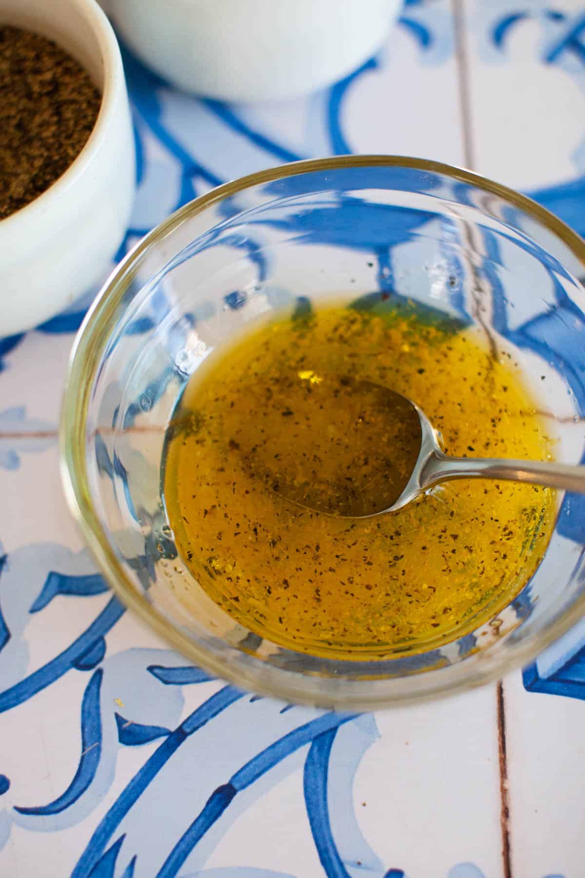 Lemon juice, olive oil, lemon zest, salt and pepper mixed together in a glass mixing bowl.