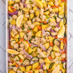Overhead photo of cooked sheet pan chicken and veggies on an aluminum baking sheet.