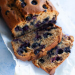 Two slices of blueberry bread positioned next to the loaf on a sheet of parchment paper.
