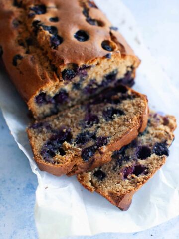 Two slices of blueberry bread positioned next to the loaf on a sheet of parchment paper.