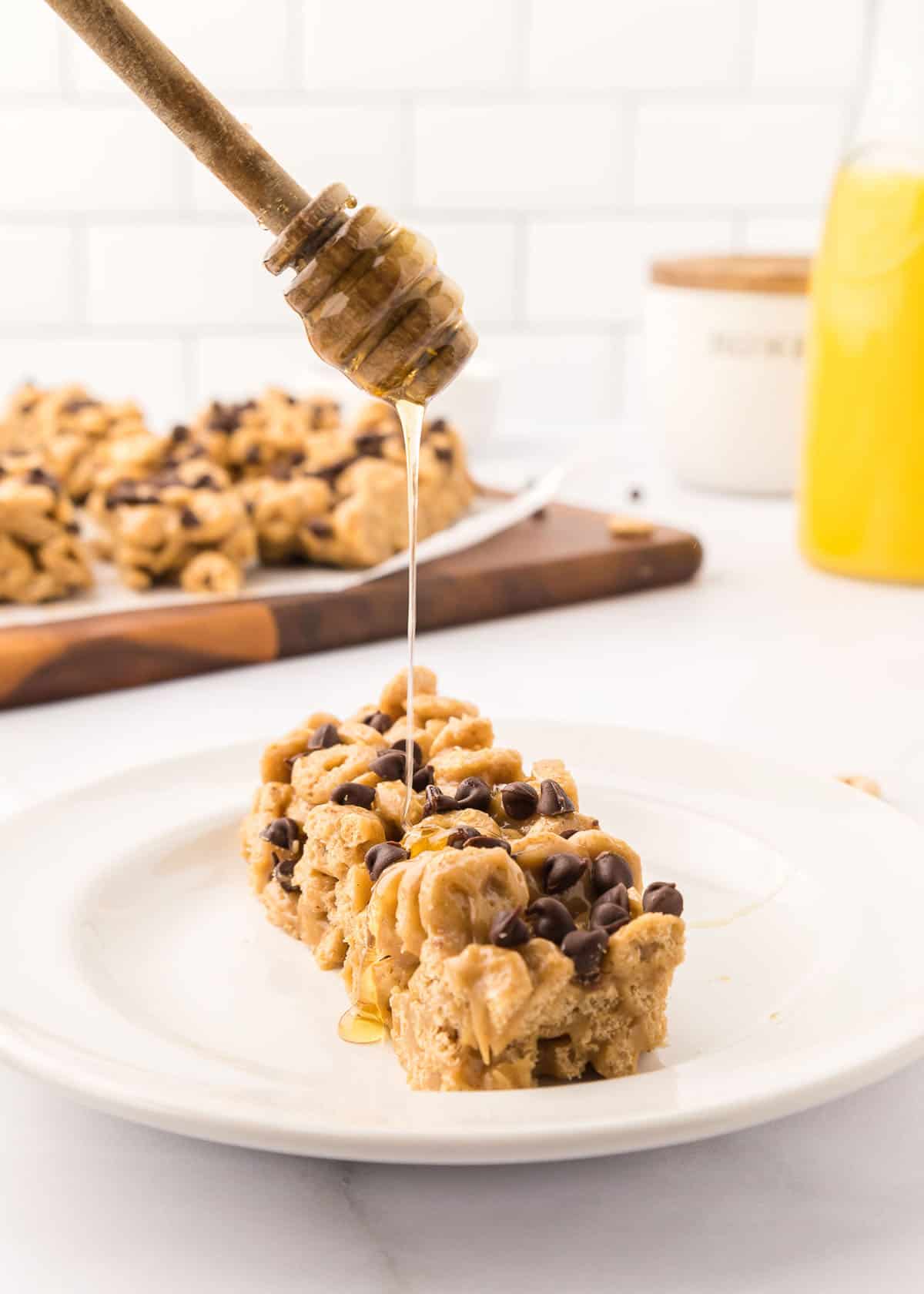 Slice of cereal bar on a small, white plate being drizzled with honey.