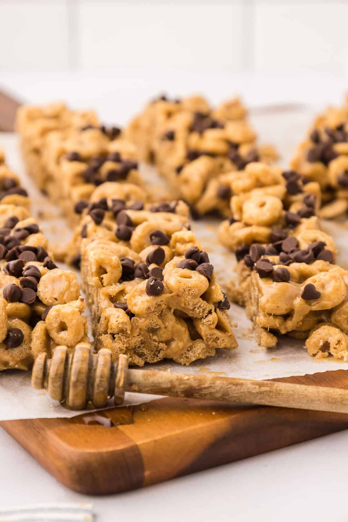 Slices of cereal bars on a wooden cutting board accented with a wooden honey dipper.