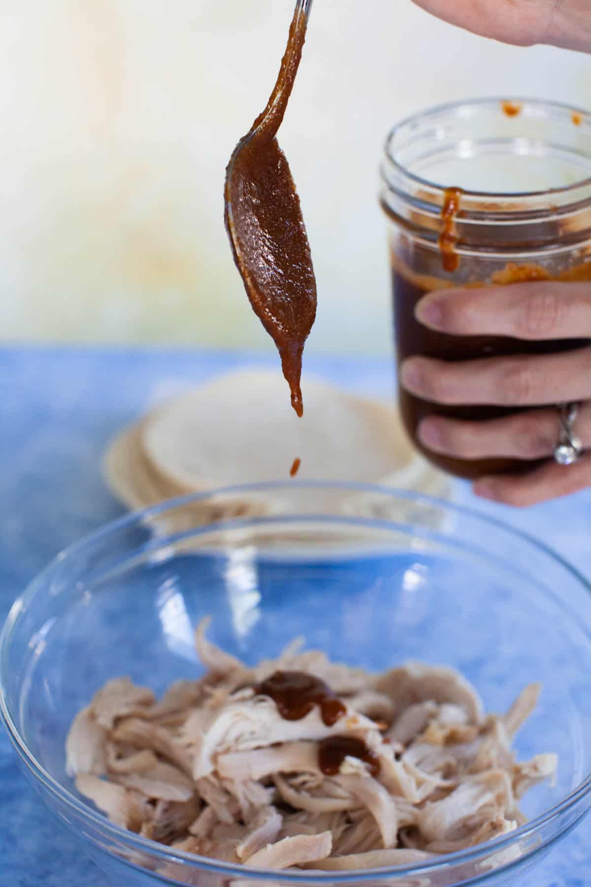 Enchilada sauce being spooned onto the pulled rotisserie chicken.