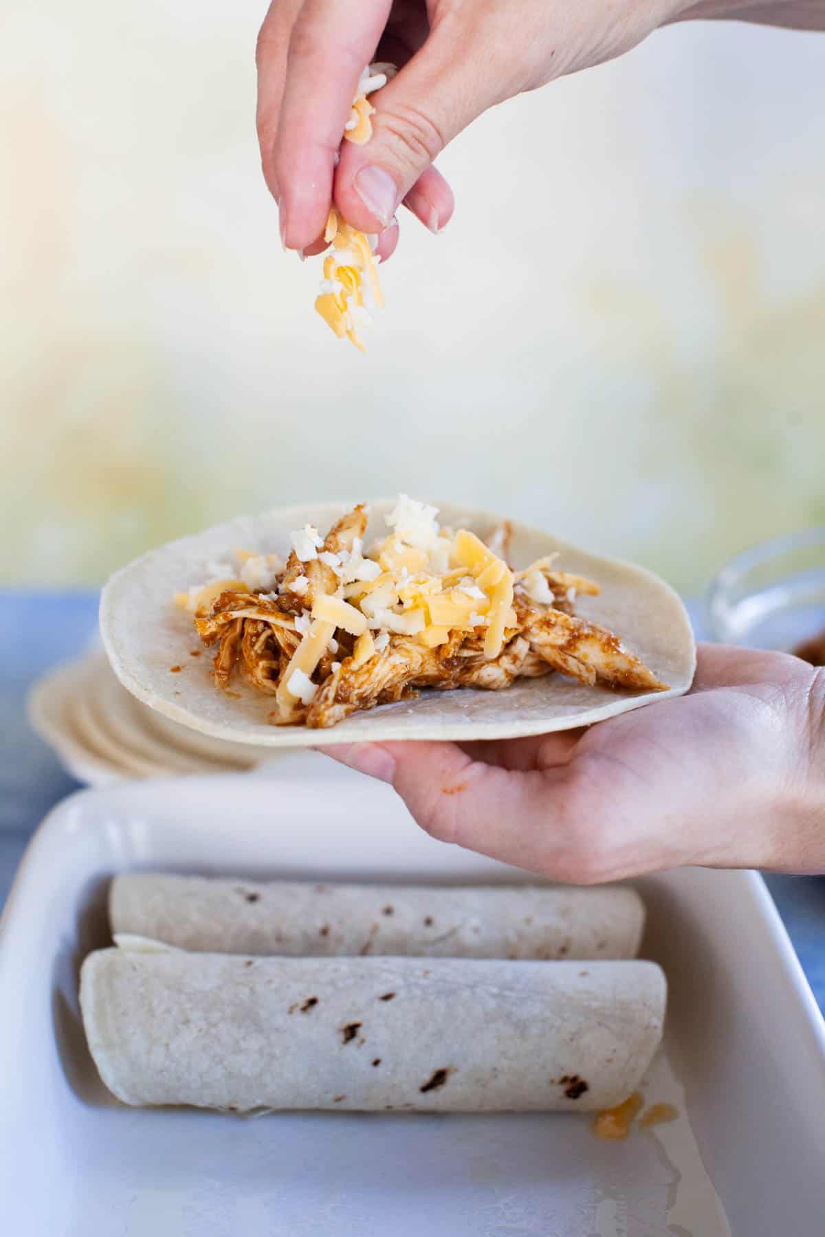 Shredded cheese being sprinkled on top of the chicken and corn tortilla.