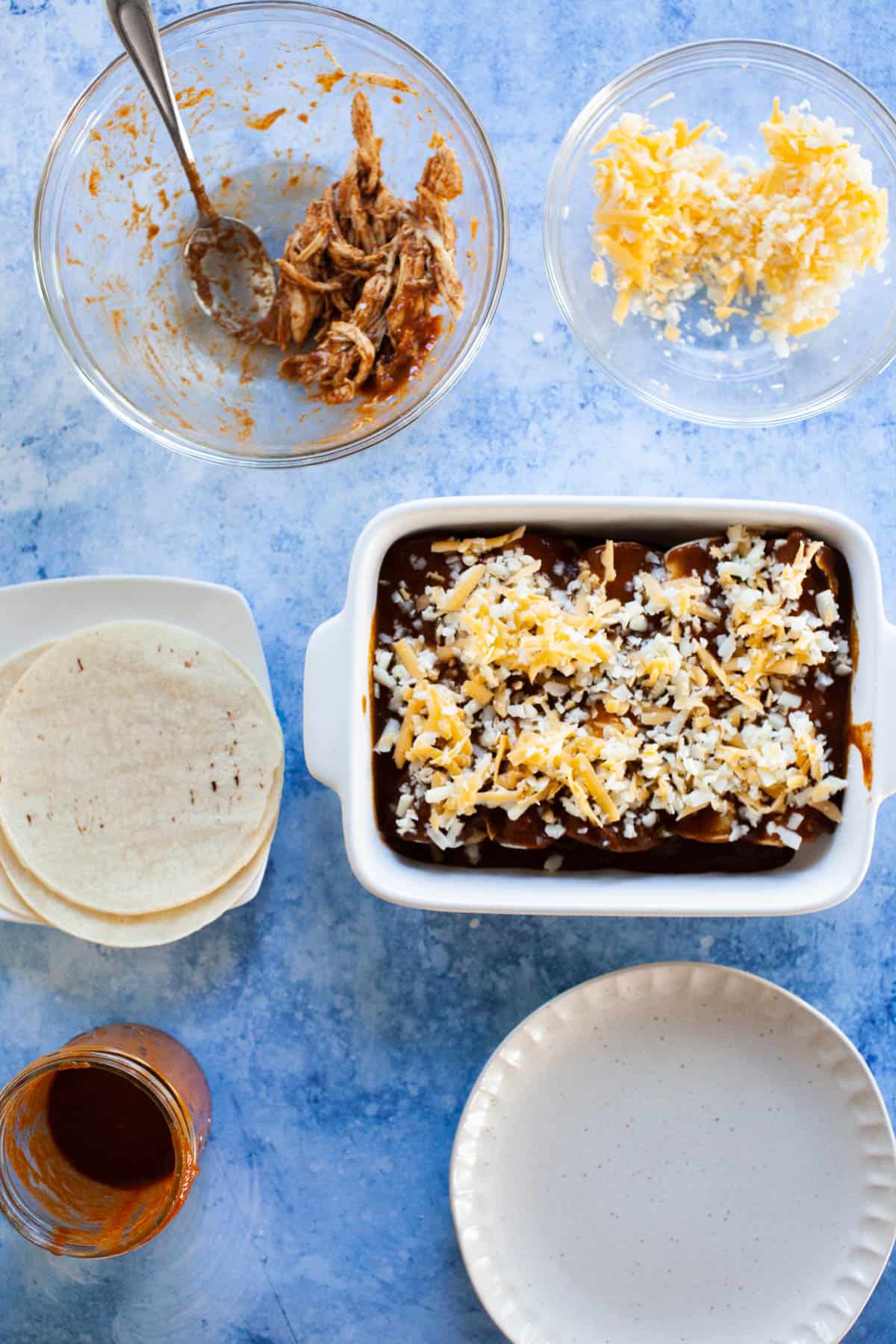 Enchiladas with sauce topped with shredded cheese.