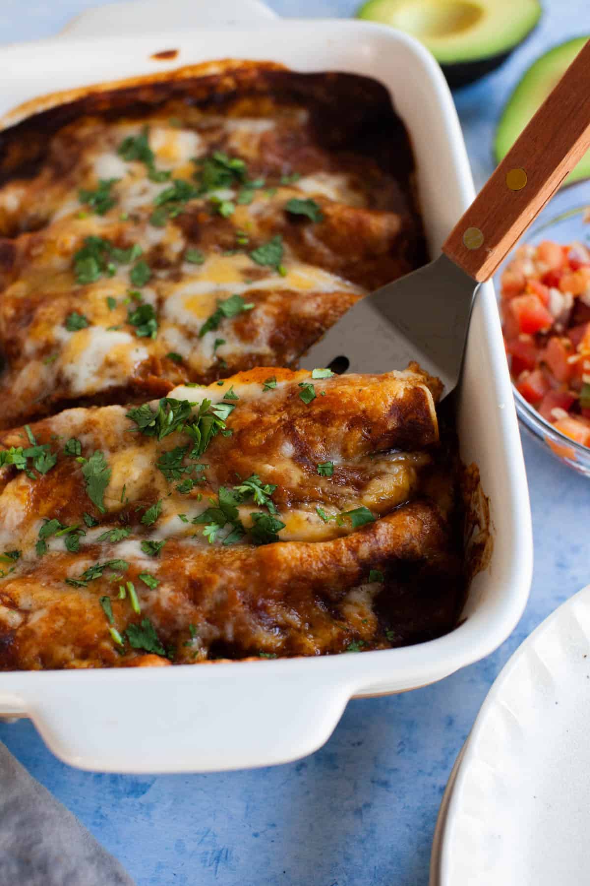 An enchilada being taking from the serving dish with a small, metal spatula.