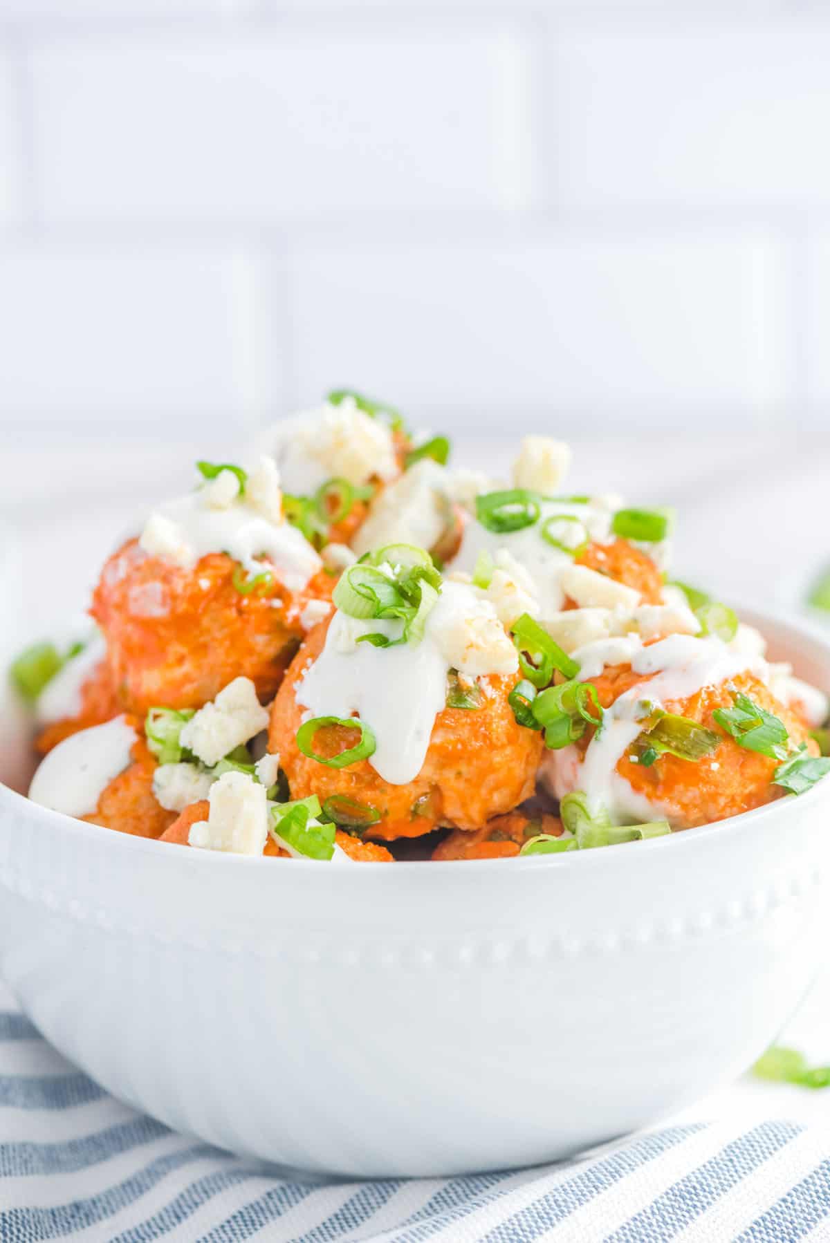Close up photo of bowl of chicken meatballs topped with ranch dressing, blue cheese crumbles and diced green onions.