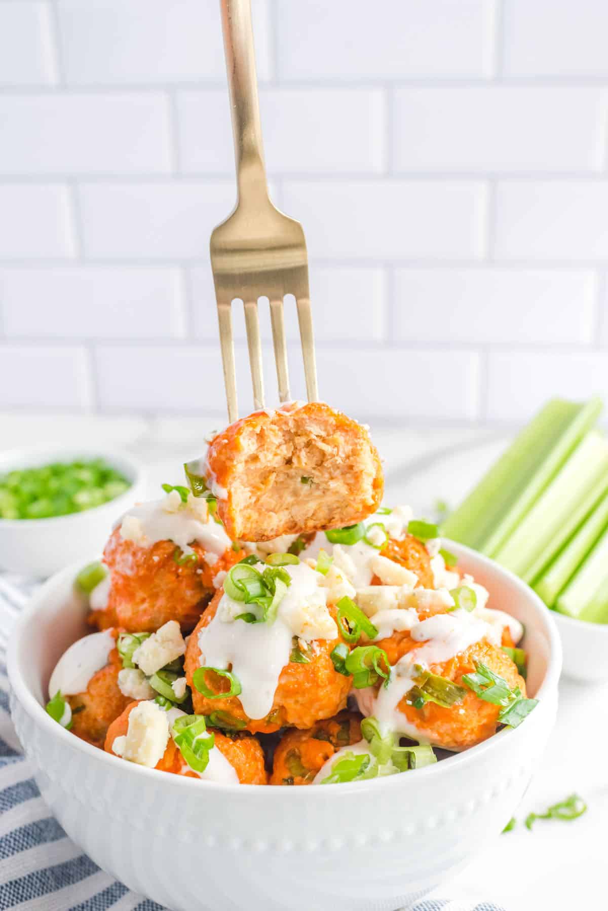 A bite taken out of one chicken meatball with the bowl of meatballs below it.
